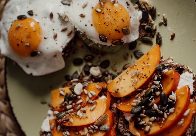 Delicious breakfast plate featuring avocado toast with fried eggs and persimmons, topped with seeds for a healthy start.